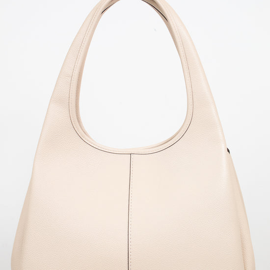 A light beige leather shoulder bag with, a vertical center seam, and a small gold logo emblem on the bottom right corner, set against a plain white background.