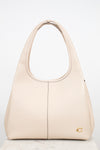 A light beige leather shoulder bag with, a vertical center seam, and a small gold logo emblem on the bottom right corner, set against a plain white background.
