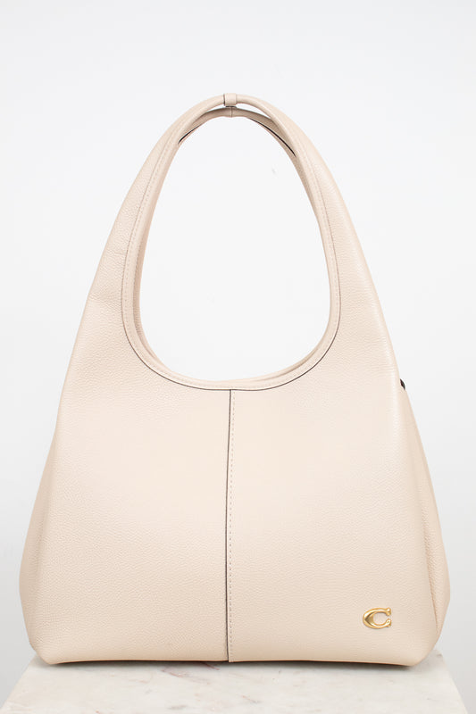 A light beige leather shoulder bag with, a vertical center seam, and a small gold logo emblem on the bottom right corner, set against a plain white background.