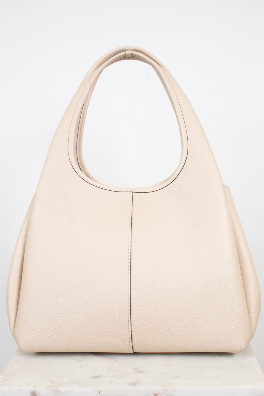Back view of a  light beige leather shoulder bag  displayed on a light marble surface against a white background.
