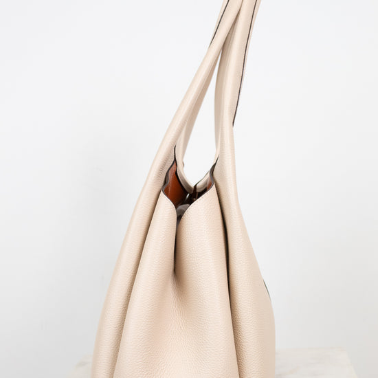 A light beige leather hobo handbag with long shoulder straps, standing upright on a light marble surface against a white background.