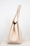 A light beige leather hobo handbag with long shoulder straps, standing upright on a light marble surface against a white background.