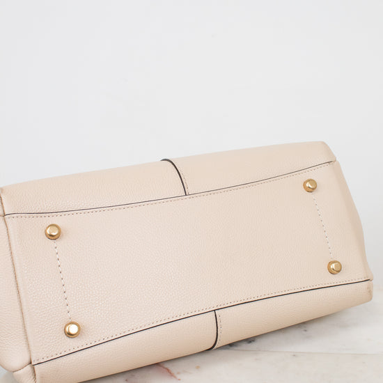 Bottom view of a beige leather shoulder bag with gold-tone metal feet, shown from a side angle on a light marble surface against a white background.