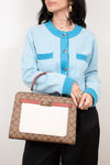 Person wearing a light blue cardigan with a patterned handbag against a plain background