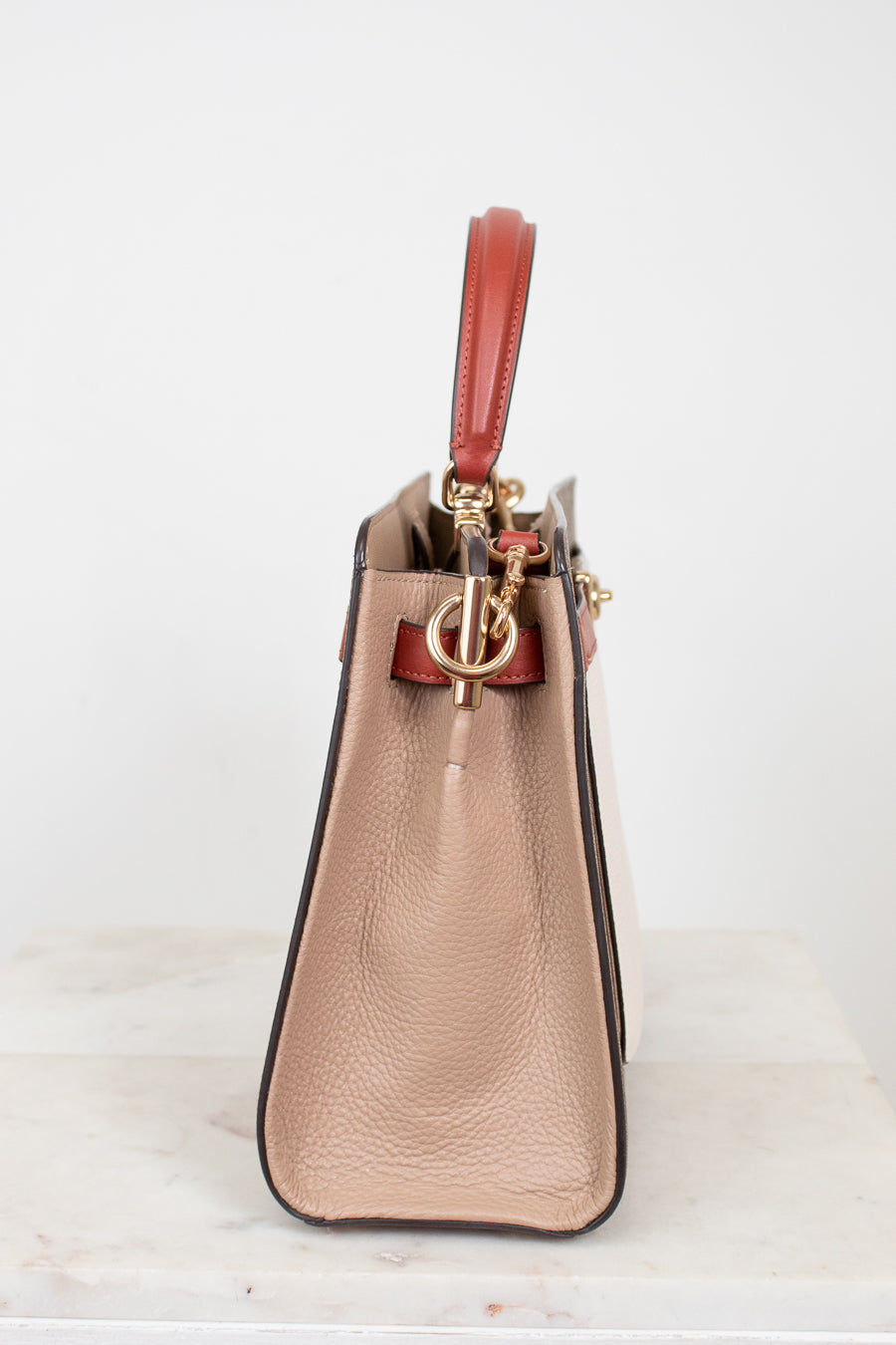 Beige handbag with a red handle on a white background