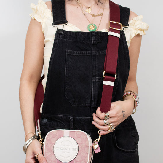 Person wearing black overalls with a pink and white striped bag