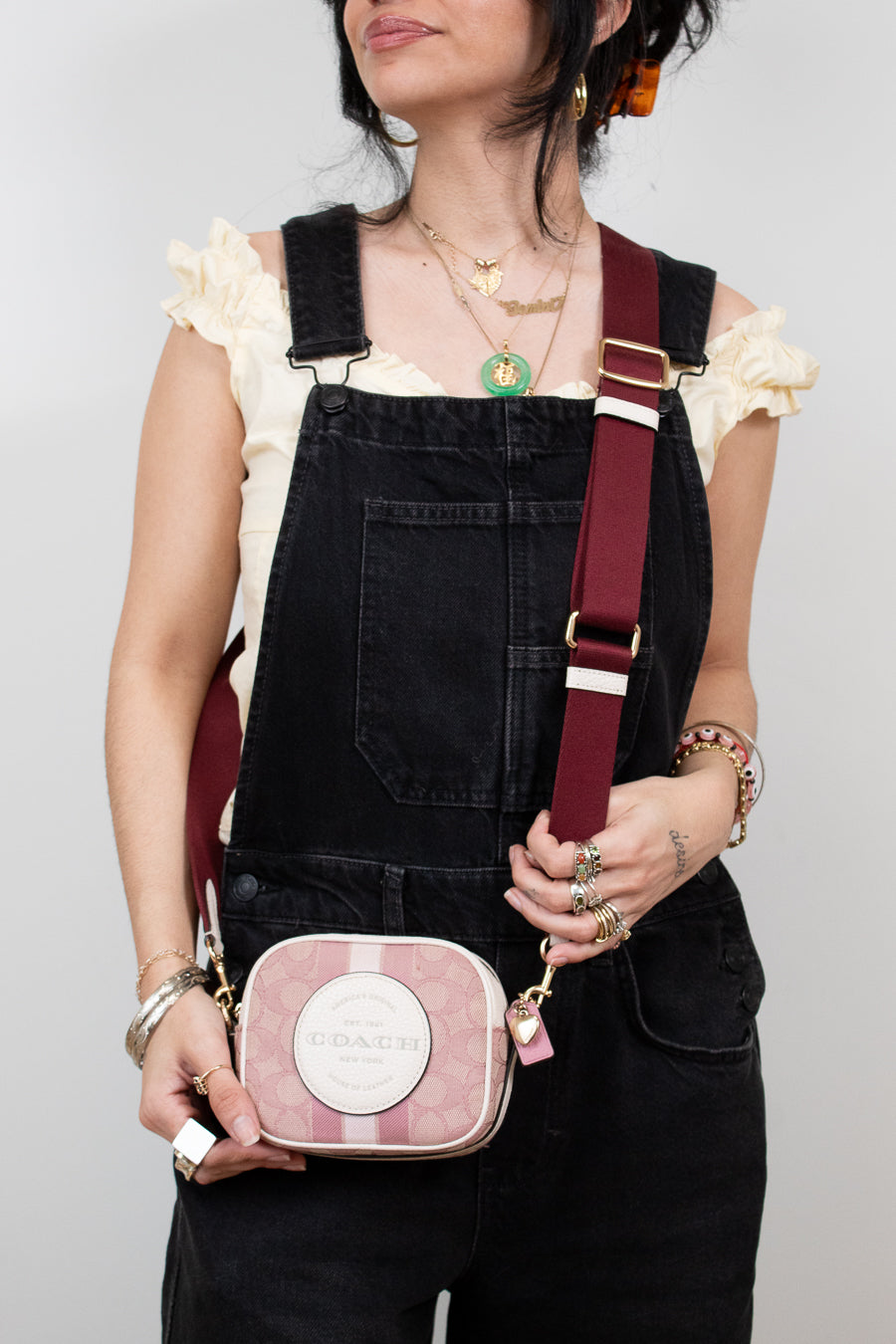 Person wearing black overalls with a pink and white striped bag