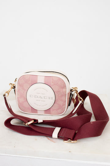 Pink and white Coach handbag with a matching strap on a light gray background