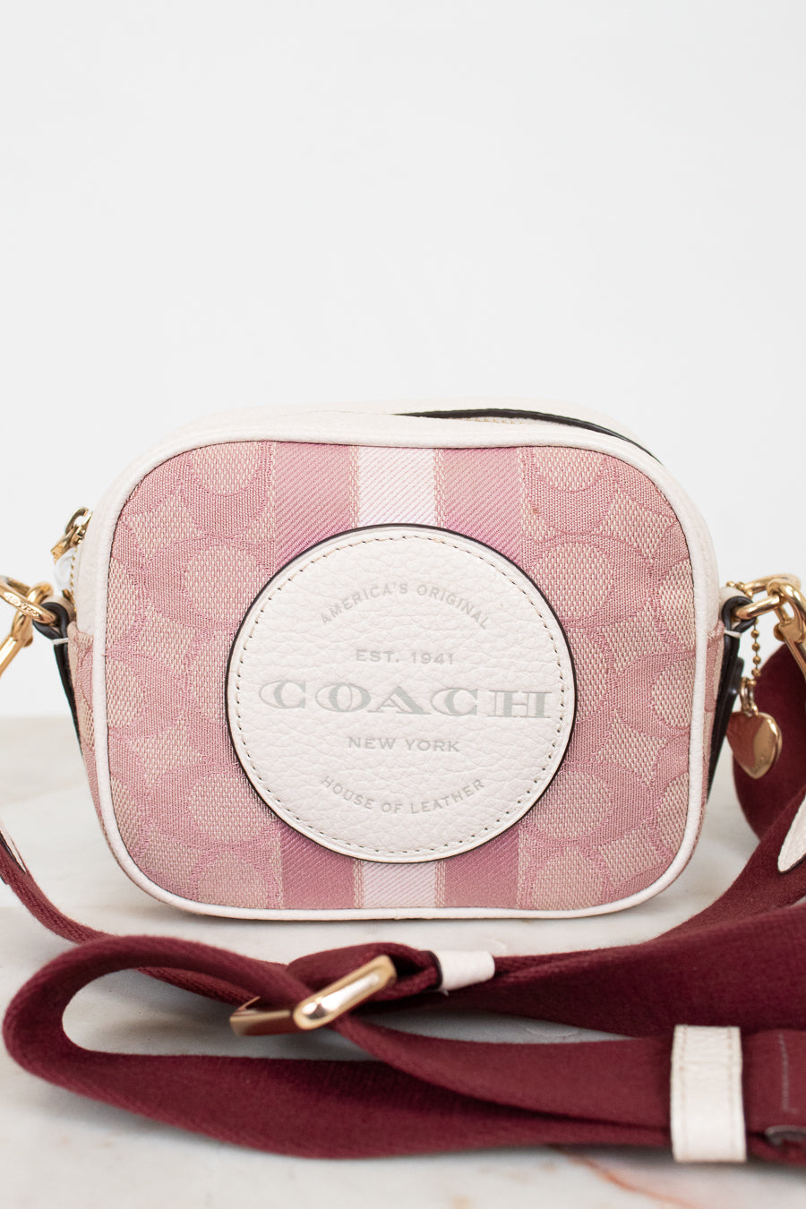 Coach handbag with pink plaid pattern and gold accents on a light background