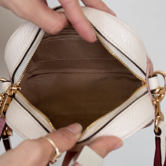 Close-up of a hand holding an open beige handbag with gold accents.