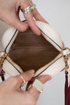 Close-up of a hand holding an open beige handbag with gold accents.