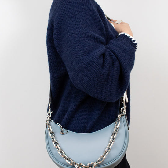 Person wearing a navy sweater holding a light blue handbag with a chain detail on a white background