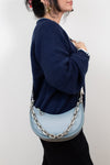 Person wearing a navy sweater holding a light blue handbag with a chain detail on a white background