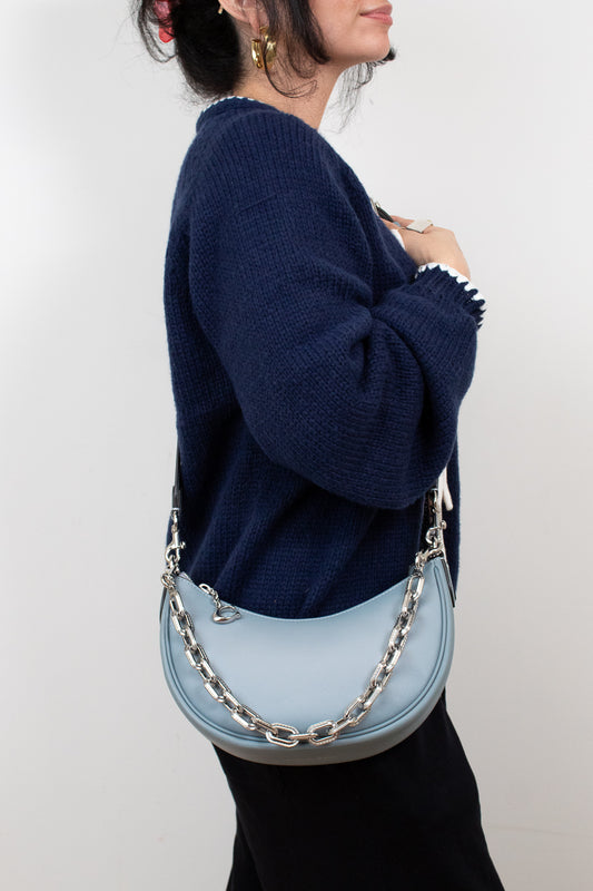 Person wearing a navy sweater holding a light blue handbag with a chain detail on a white background