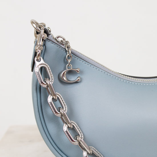 Light blue handbag with a silver chain detail on a white background