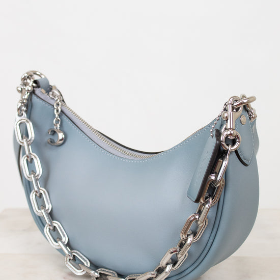 Light blue handbag with a silver chain on a white background