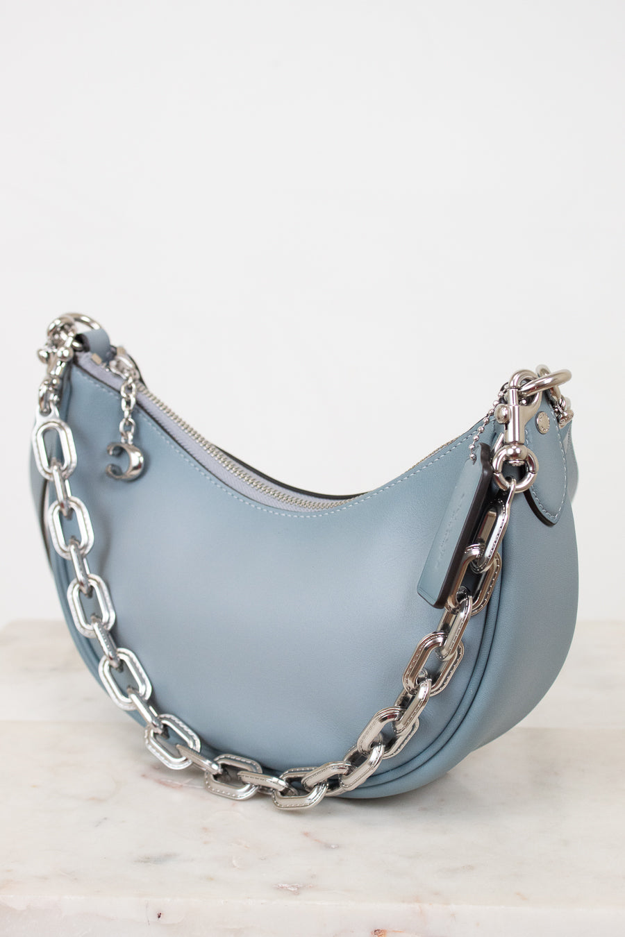 Light blue handbag with a silver chain on a white background