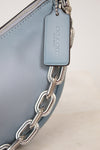 Close-up of a Coach handbag with a silver chain detail on a light background