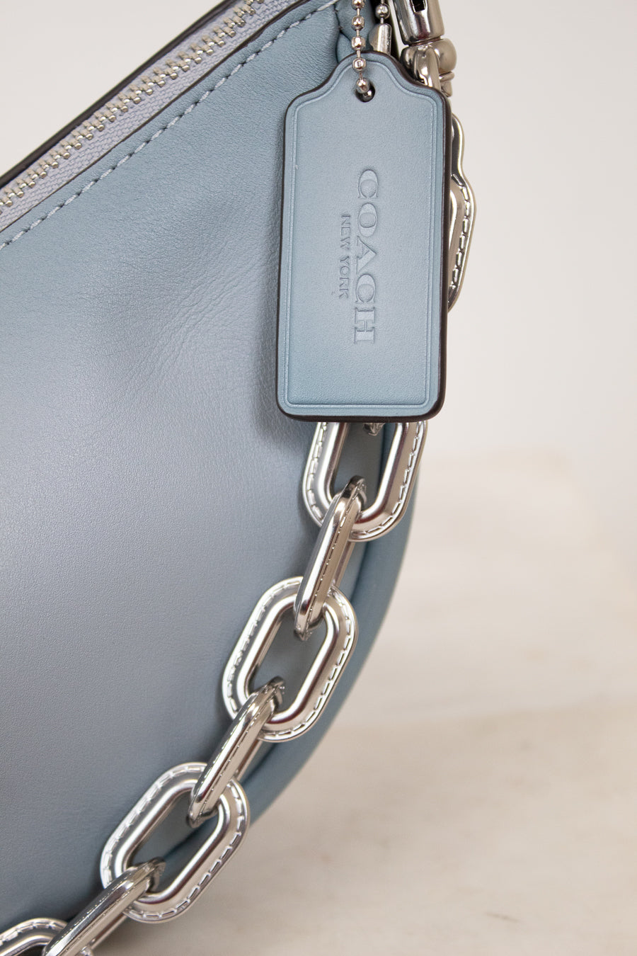 Close-up of a Coach handbag with a silver chain detail on a light background