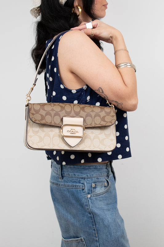Person wearing a polka dot top and holding a Coach handbag against a plain background