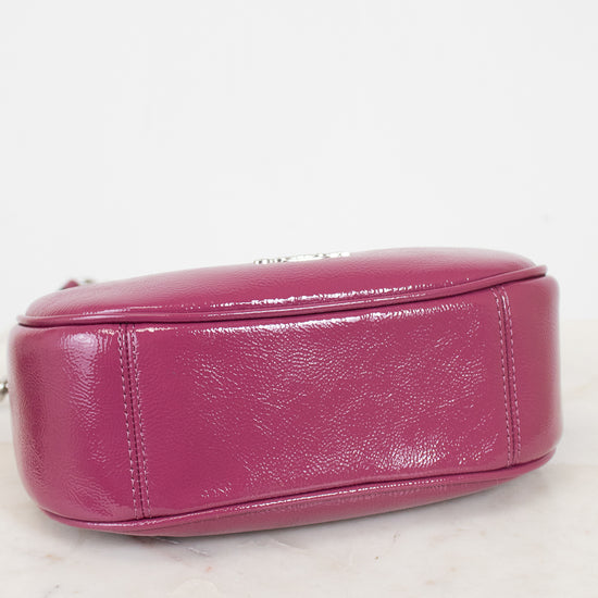 A close-up of a magenta pink leather handbag showing the bottom and side panel with silver-tone hardware on a white marble surface against a white background.