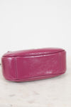 A close-up of a magenta pink leather handbag showing the bottom and side panel with silver-tone hardware on a white marble surface against a white background.