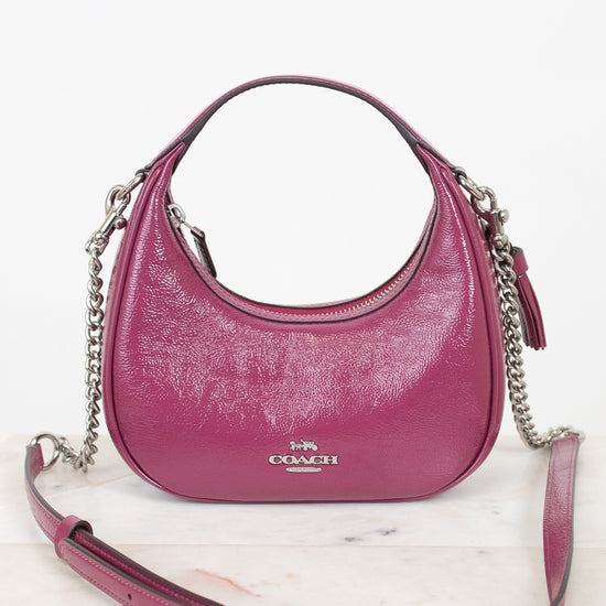 A pink Coach hobo shoulder bag with silver chain straps, displayed on a light marble surface against a white background.