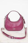 A pink Coach hobo shoulder bag with silver chain straps, displayed on a light marble surface against a white background.