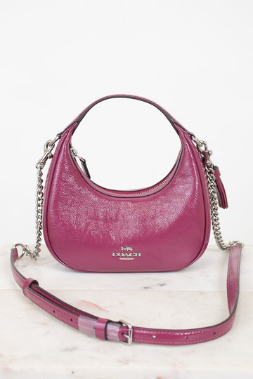 A pink Coach hobo shoulder bag with silver chain straps, displayed on a light marble surface against a white background.