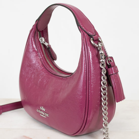 A magenta pink pebbled leather shoulder bag by Coach, featuring a silver-tone chain strap, a tassel detail, and a silver-tone logo on the front, set against a clean white background.