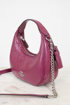 A magenta pink pebbled leather shoulder bag by Coach, featuring a silver-tone chain strap, a tassel detail, and a silver-tone logo on the front, set against a clean white background.