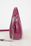 A side profile view of a magenta pebbled leather shoulder bag with a silver chain strap and tassel detail, set against a plain white background.