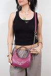 A woman wearing a black ribbed tank top and gray pants holds a pink Coach crescent shoulder bag with a chain strap. The Coach logo is visible on the front of the bag.