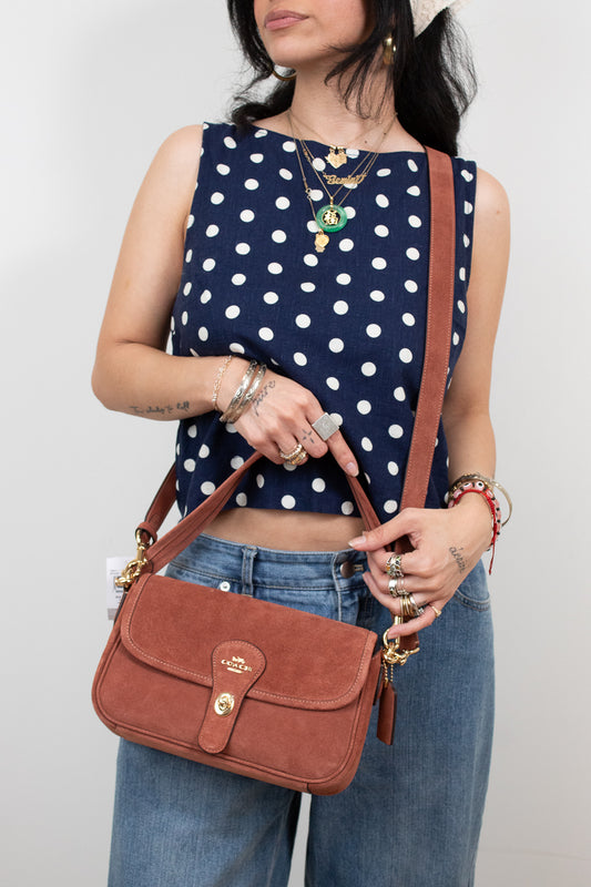 Person wearing a navy blue top with white polka dots and holding a mauve handbag.