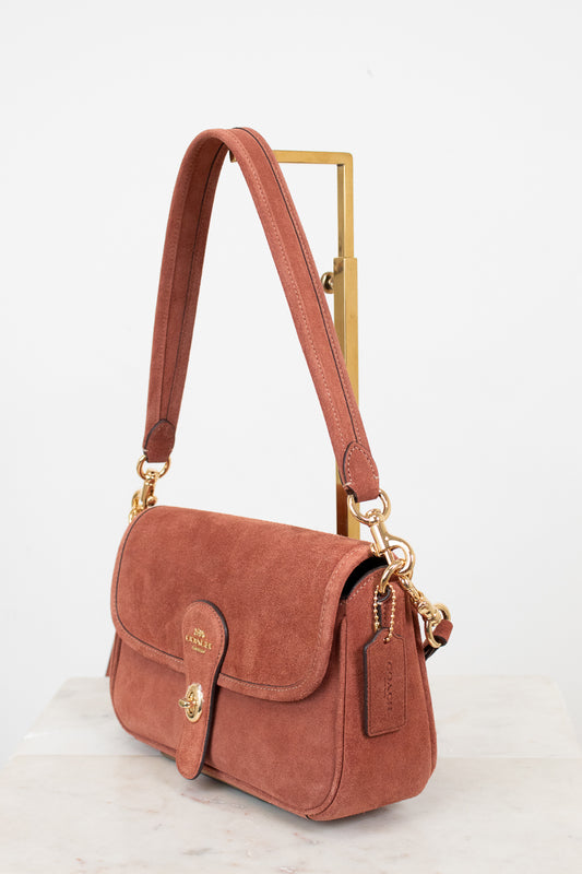 Mauve suede handbag with gold accents on a white background