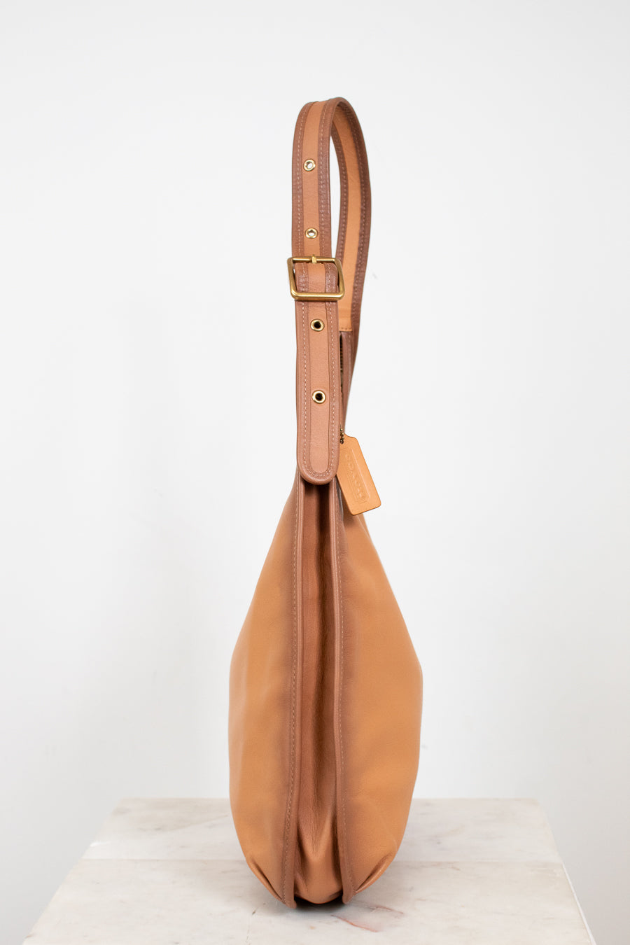 Tan leather handbag with a strap on a white background