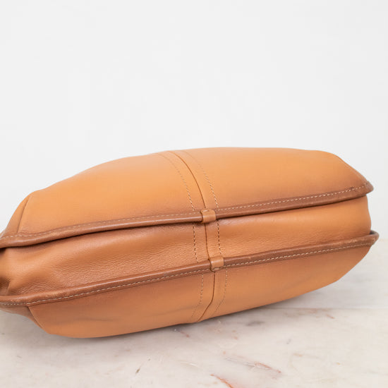 Tan leather purse on a light wooden surface with a white background