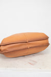 Tan leather purse on a light wooden surface with a white background