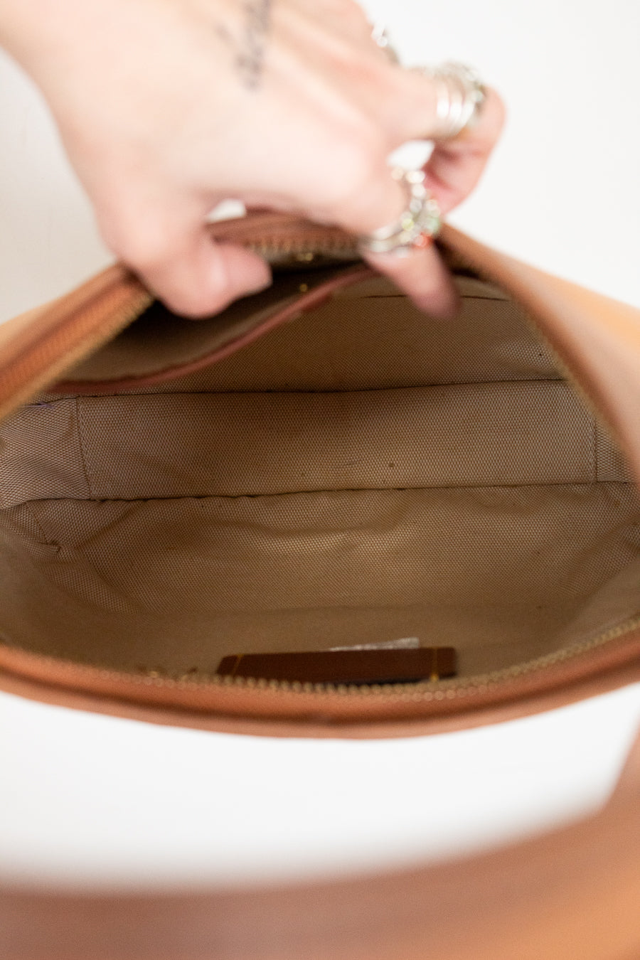 Close-up of a hand holding a brown leather bag with a white background