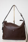  A dark brown leather shoulder bag with a soft, slouchy silhouette with a adjustable strap with silver hardware , the bag is photographed upright on a white background hanging from a gold hardware stand.