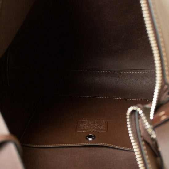 Close-up of the interior of a brown leather handbag, showing the dark brown lining, silver-tone zipper, and a small embossed brand patch on the bottom.