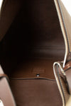 Close-up of the interior of a brown leather handbag, showing the dark brown lining, silver-tone zipper, and a small embossed brand patch on the bottom.