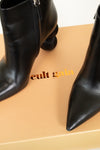 Black leather ankle boots with pointed toes and stacked block heels, displayed on a beige box with the brand name 'cult gaia' printed on it.