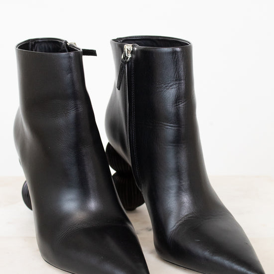 A pair of black leather pointed-toe ankle boots with side zippers, displayed on a light marble surface against a white background.