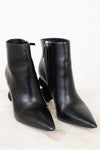 A pair of black leather pointed-toe ankle boots with side zippers, displayed on a light marble surface against a white background.