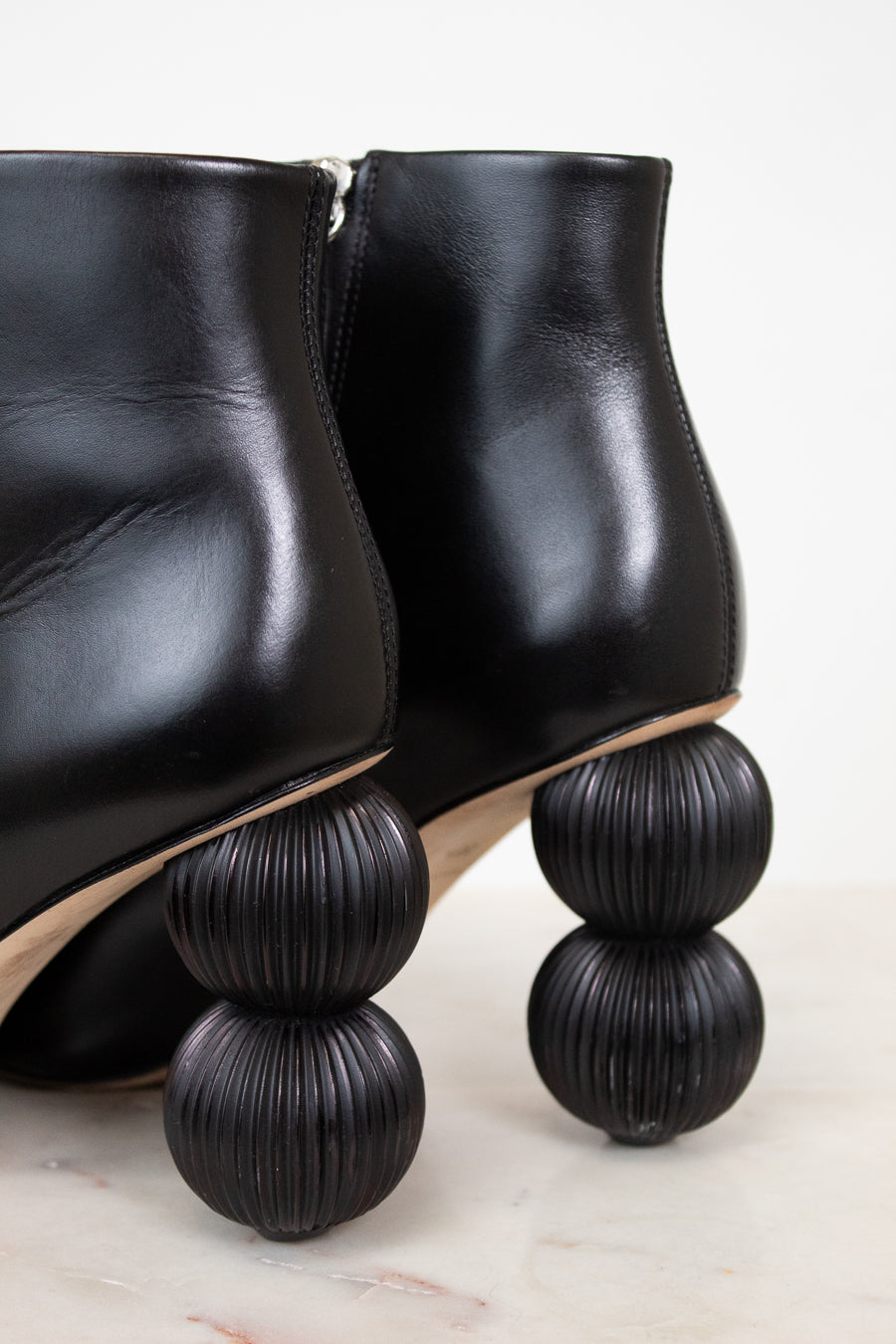 Black leather ankle boots with distinctive stacked spherical black heels, shown on a light marble surface against a white background.