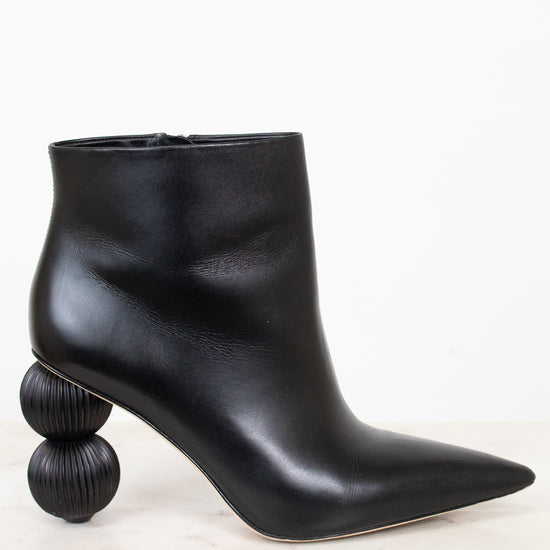 A black leather ankle boot with a pointed toe and a unique stacked spherical heel, displayed on a light marble surface against a white background.