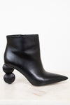 A black leather ankle boot with a pointed toe and a unique stacked spherical heel, displayed on a light marble surface against a white background.