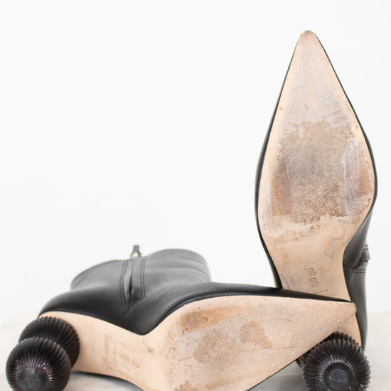A pair of black leather high-heeled boots with sculptural, wheel-like beige and brown platform soles, photographed on a white background.