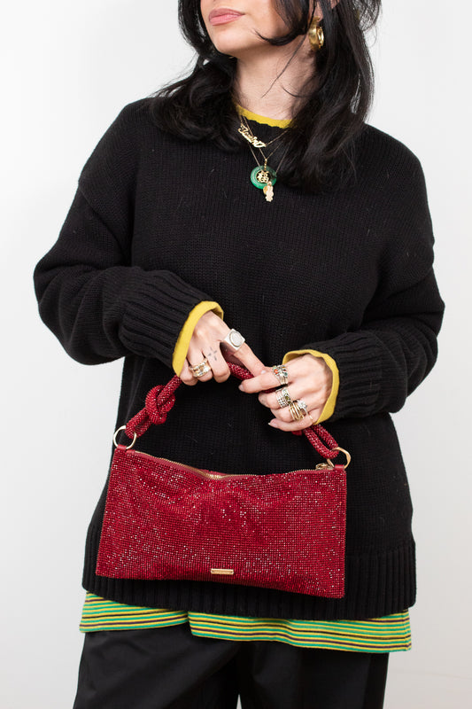 Person holding a red rhinestone detailed handbag against a white background